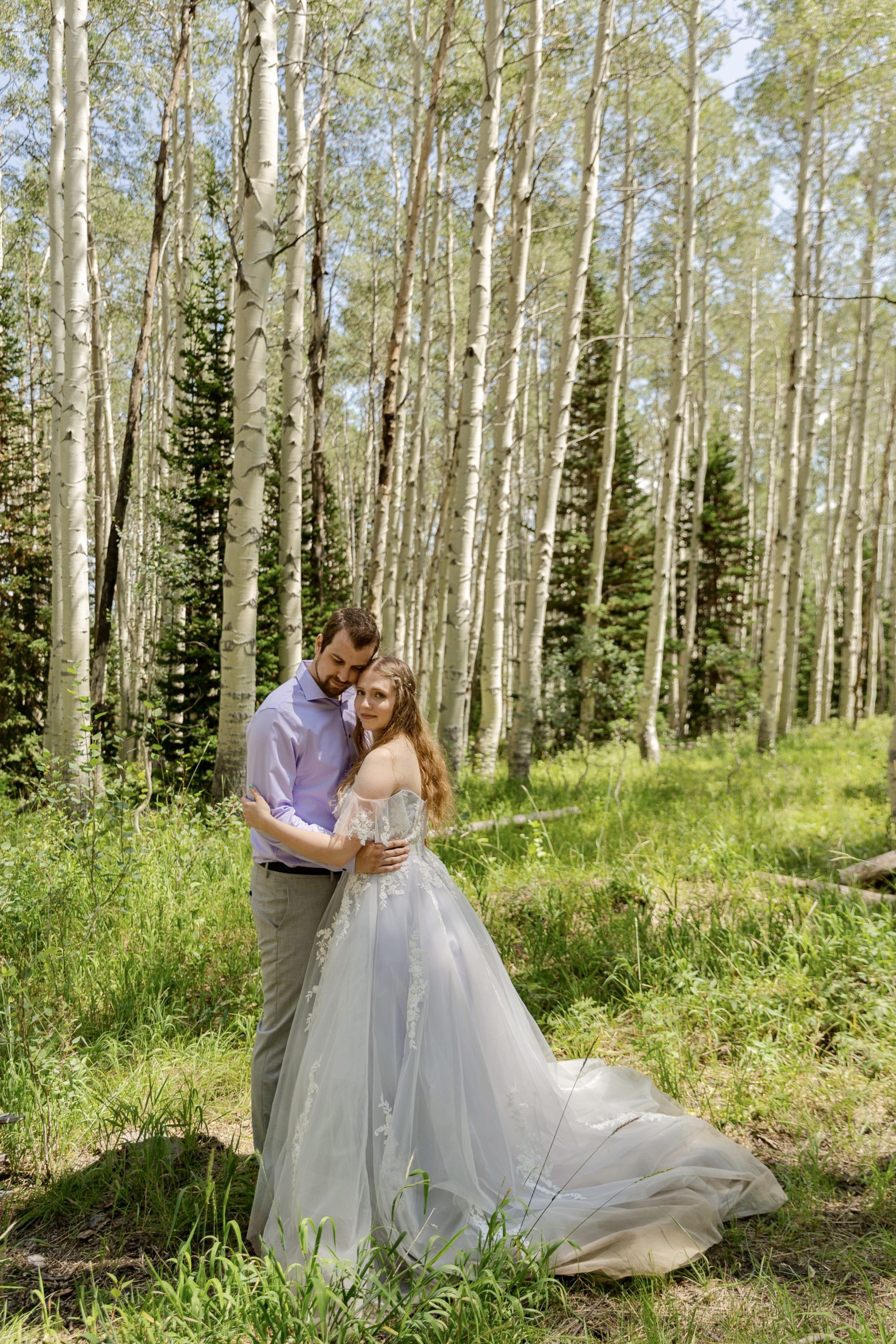 Bride and groom embracing each other in a forest of green aspen trees in the summer