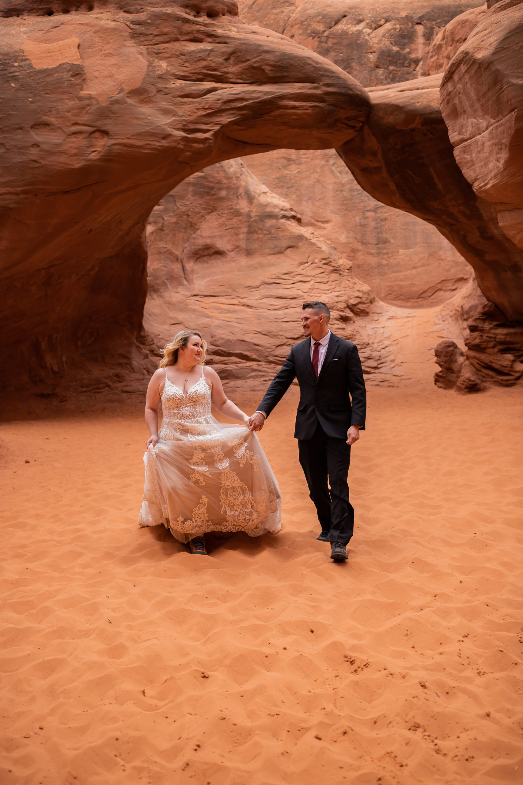 Bride and groom walking towards camera in front of Sand Dune Arch in Arches National Park in Moab, Utah