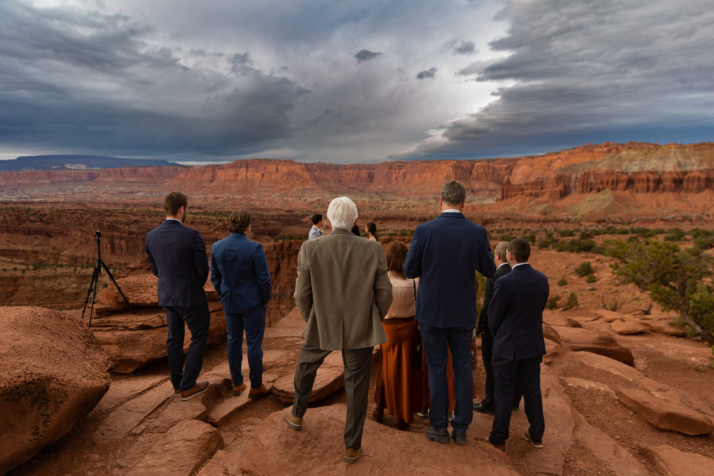 Guests standing on a red rock cliffside watching their loved ones get married.