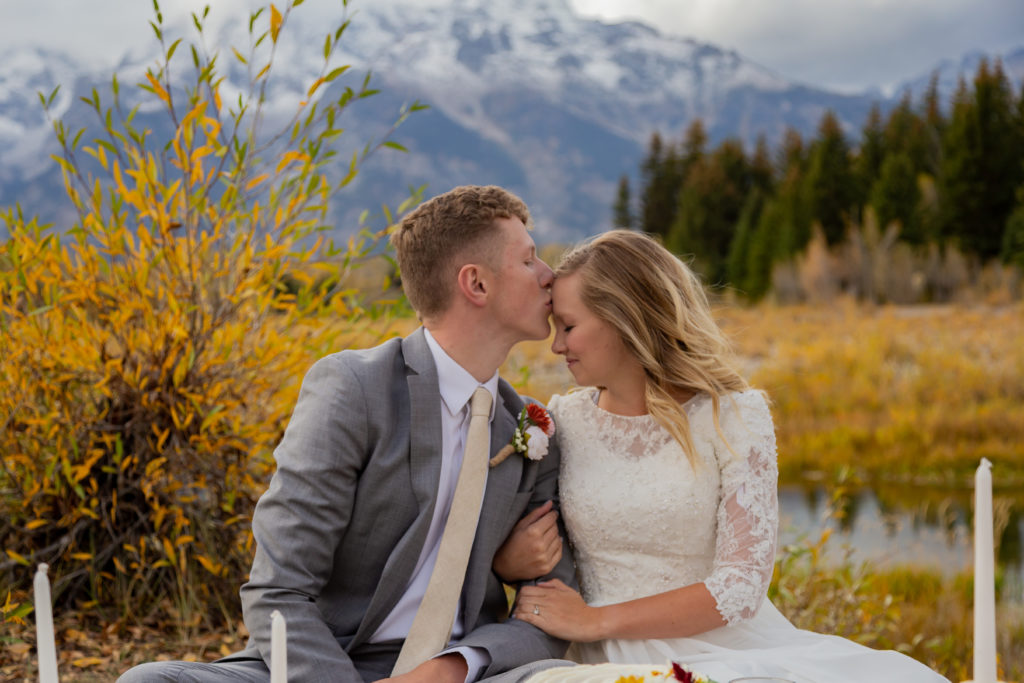 Groom kissing his bride's forehead with the Teton mountain range behind them in Grand Teton National Park in Wyoming.