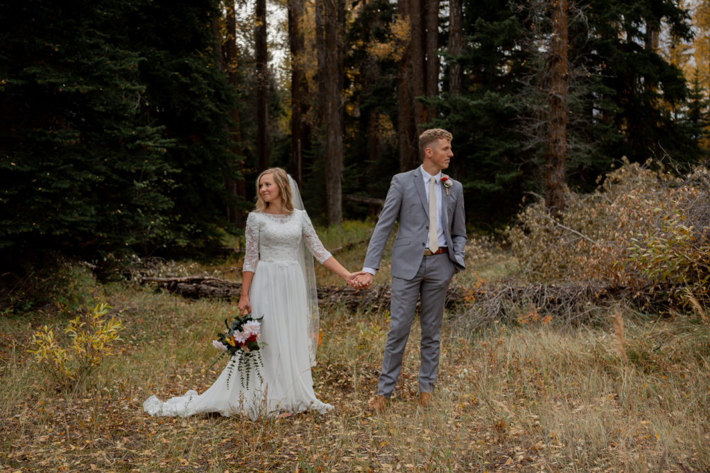 Grand Teton National Park Elopement. Couple standing in a forest with fall colors, side-by-side holding hands and looking away from each other.