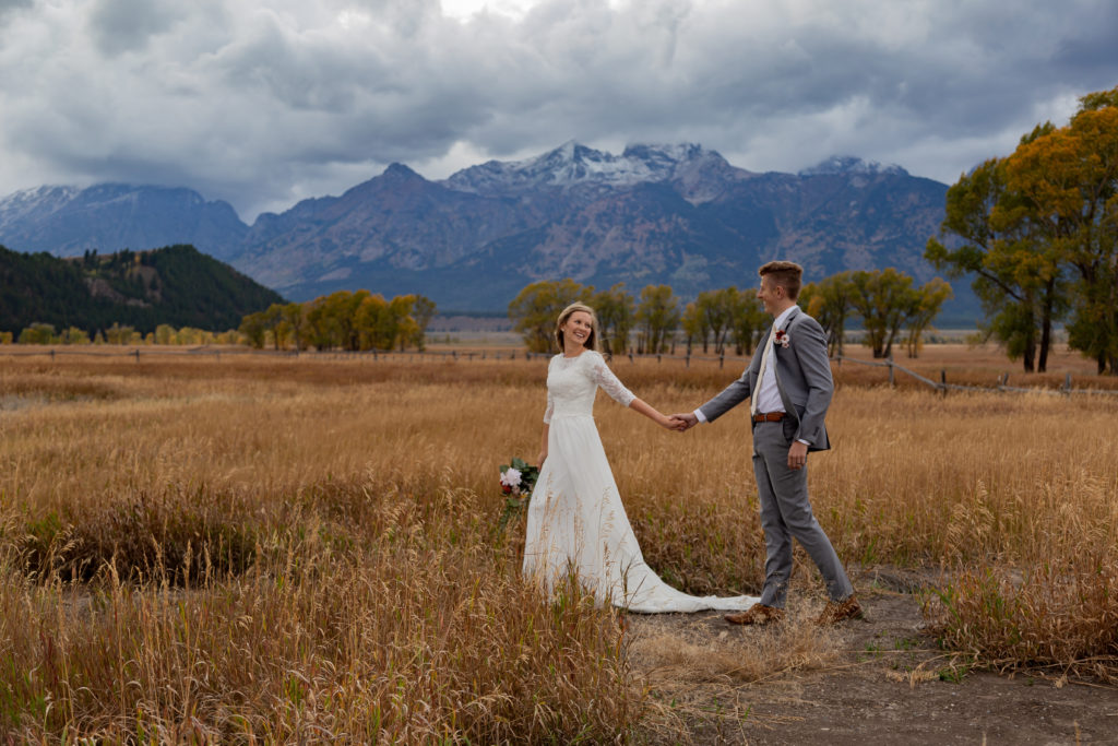 Bride leading her groom across a field with the Teton Mountains behind them at Grand Teton National Park in Wyoming.