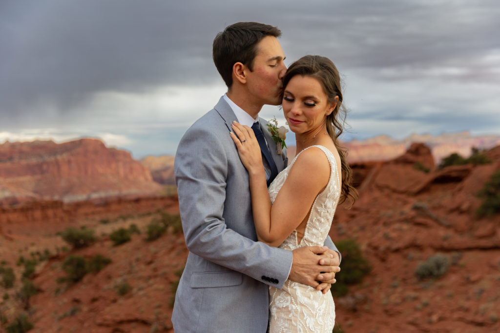Bride and groom embracing each other, groom kissing bride's head in Capitol Reef National Park