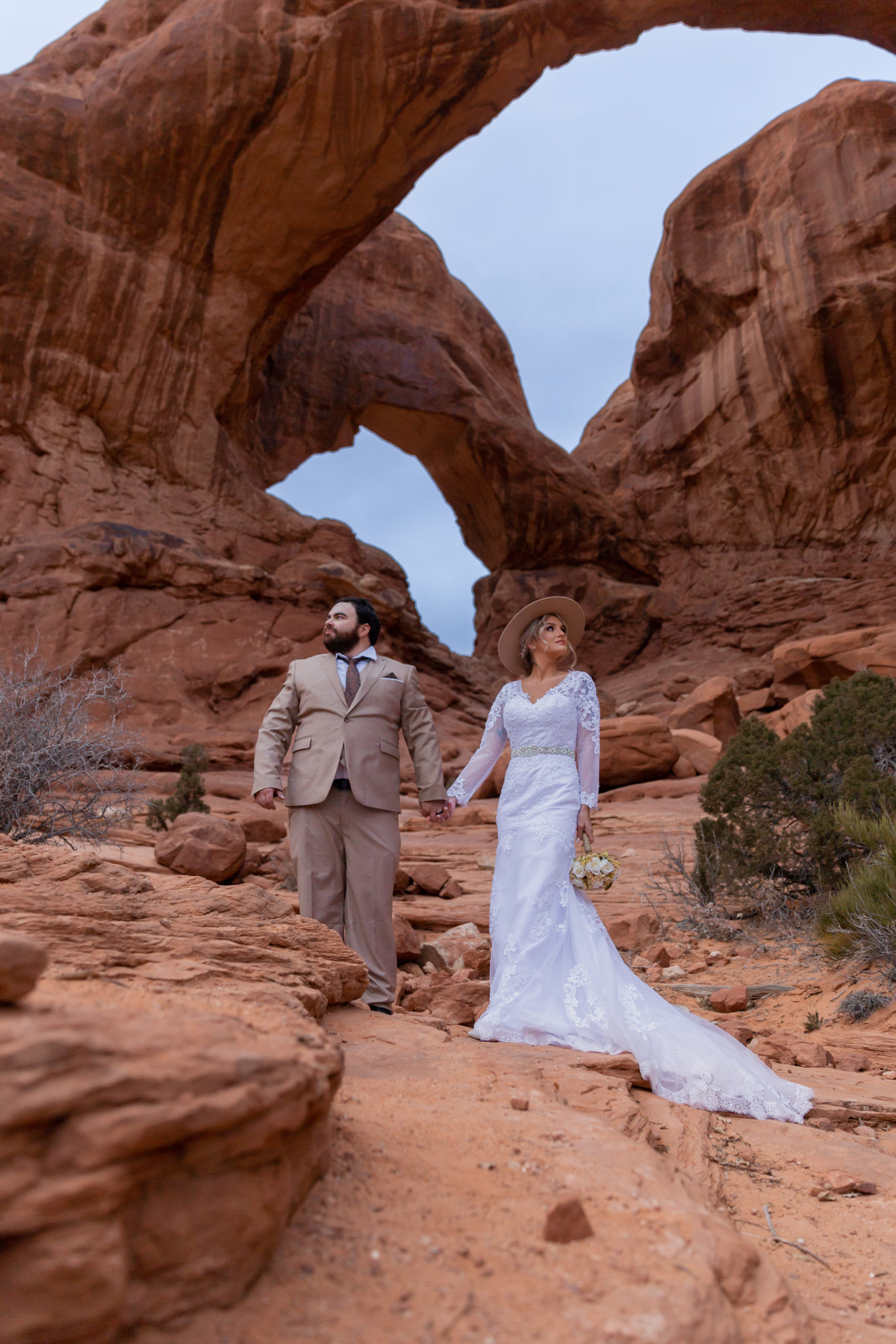 Bride and groom standing under Double Arch in Arches National Park in Moab, Utah