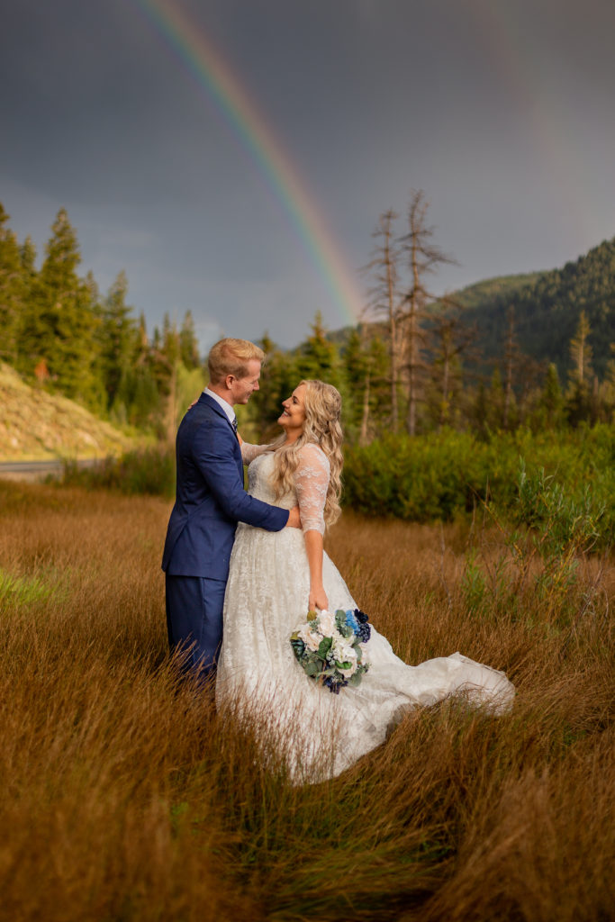 Mountain Elopement Locations Near Salt Lake - bride and groom embracing each other during a stormy evening in the mountains with a rainbow in the sky