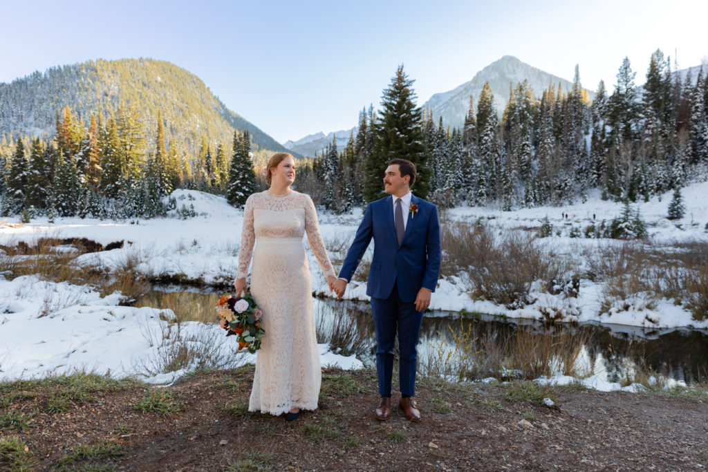 Mountain Elopement Locations Near Salt Lake - bride and groom stand in front of snowy mountains in Big Cottonwood Canyon holding hands