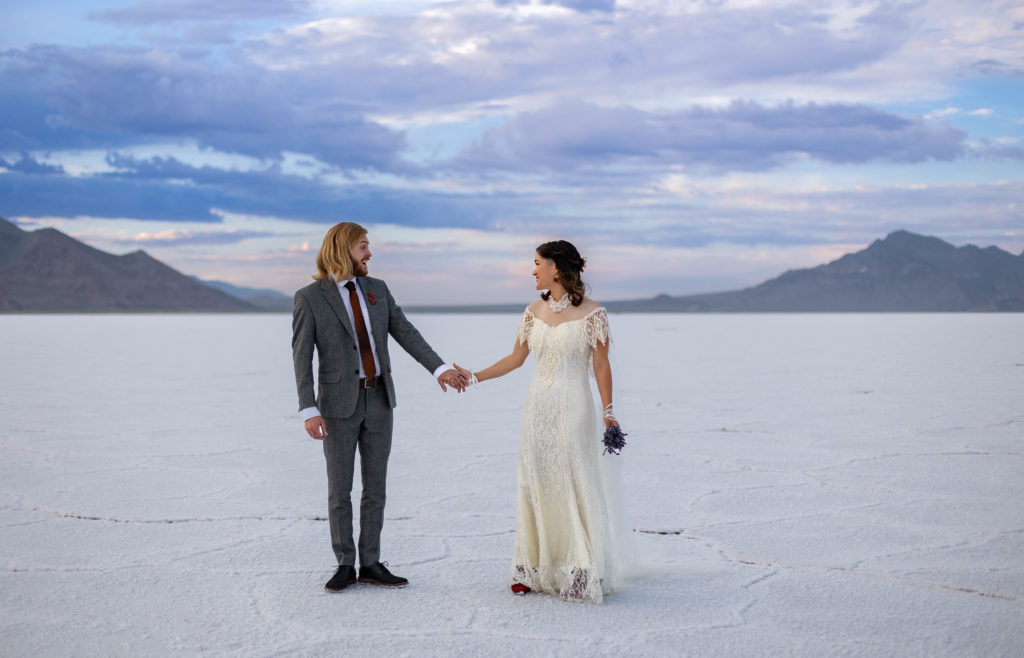 Bonneville Salt Flats Utah Wedding photos. Bride and groom are holding hands and just turned around to face each other and see each other in their wedding attire for the first time.