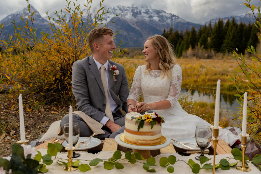 Fall Elopement in Grand Teton National Park in Jackson Hole, Wyoming. Bride and groom are sitting in front of a cake picnic setup in front of the Teton mountain range.