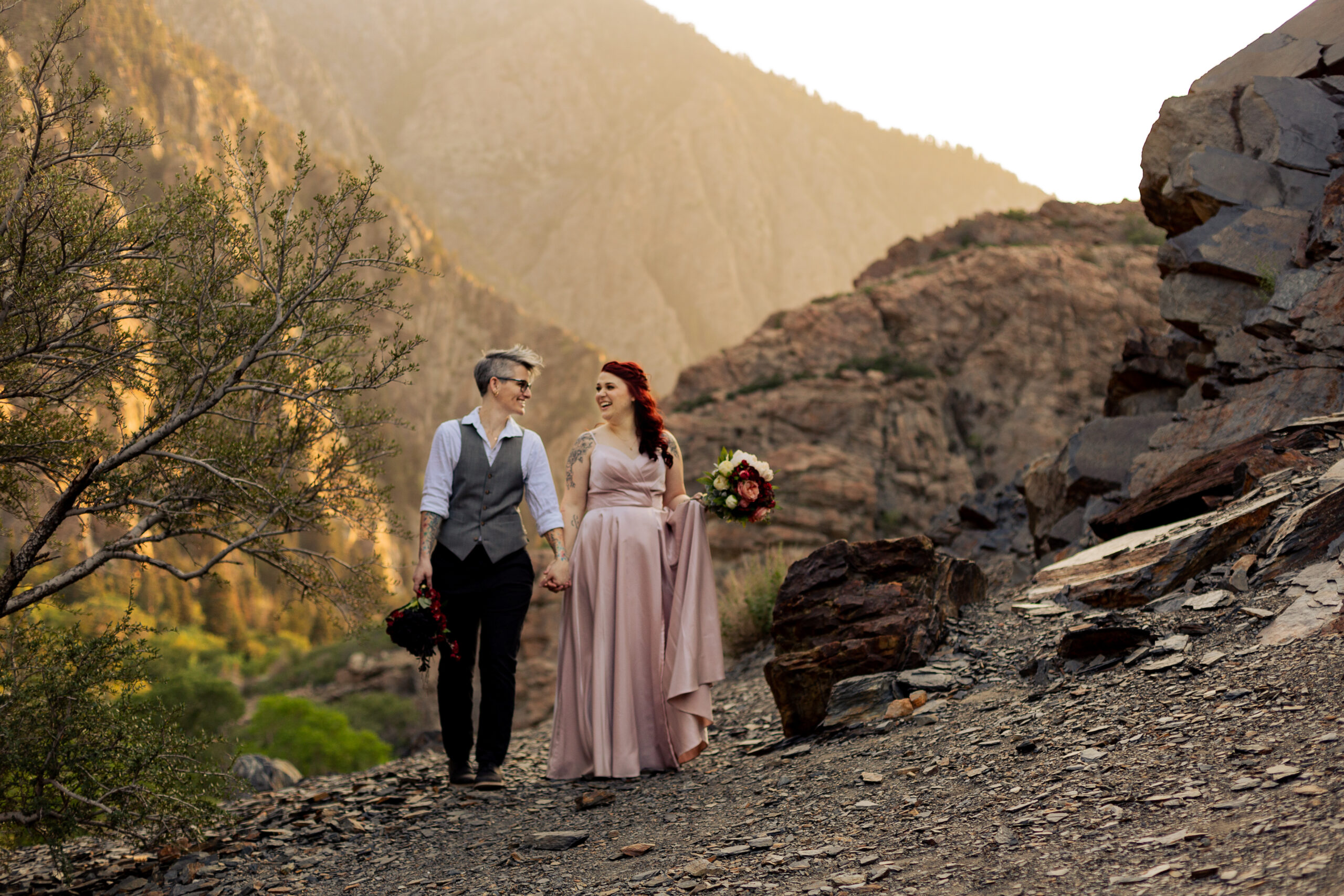 LGBTQIA+ mountain elopement in Salt Lake City, Utah with two brides holding hands while walking towards the camera and smiling at each other.