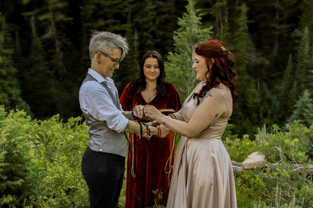 LGBTQIA+ mountain elopement in Salt Lake City, Utah with two brides standing in front of their officiant during their hand fasting ceremony.