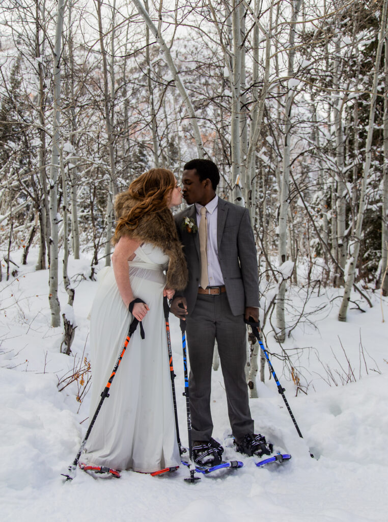 Bride and groom snowshoeing and taking a moment for a kiss.