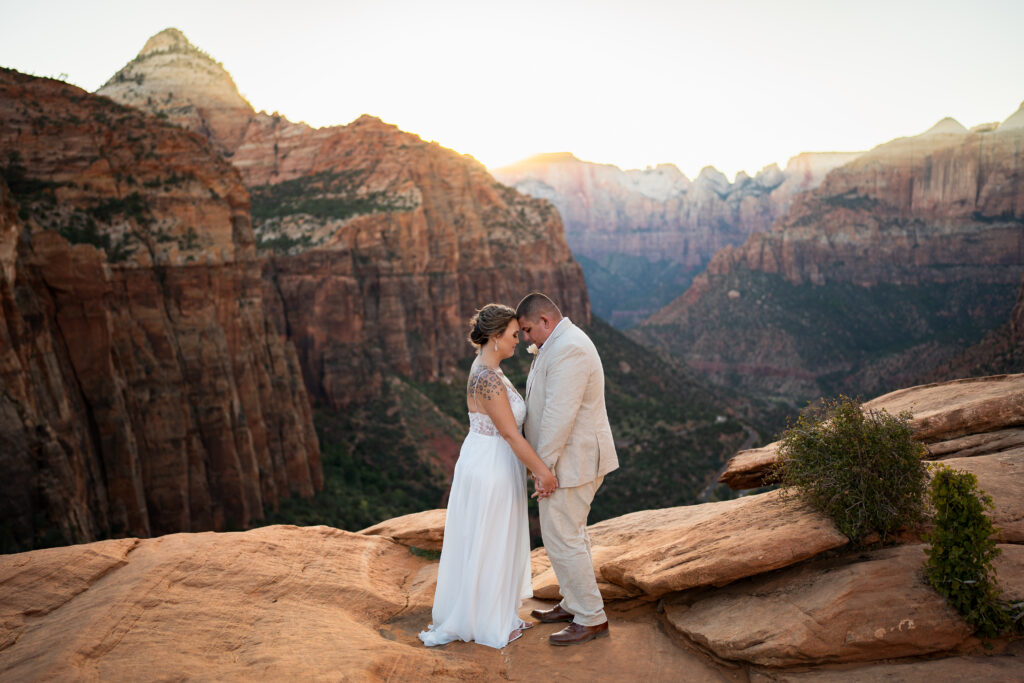 Elopement with Bride and Groom facing each other and holding hands with foreheads together in Zion National Park in Utah at Canyon View Overlook at Sunset