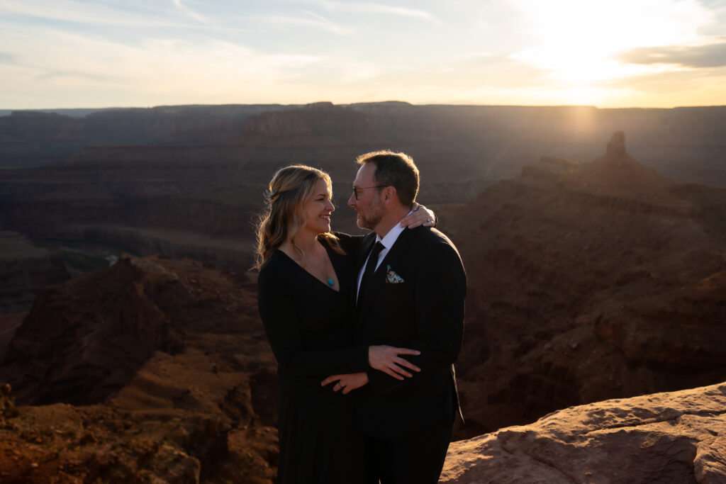 Bride and groom wearing all black facing each other and embracing one another overlooking Dead Horse Point in Moab, Utah