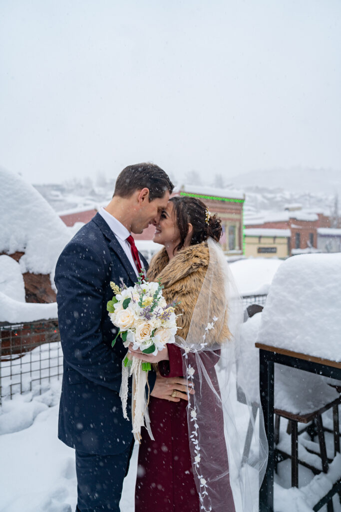 Bride and groom standing outside on the deck of the bar in the snow as snow is falling in Park City, Utah