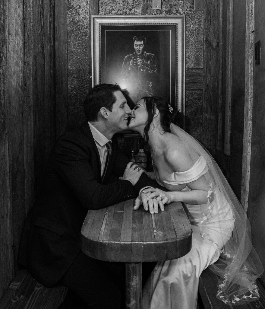 Black and white photo of bride and groom sitting across from each other and holding hands at a table in a bar in Park City, Utah