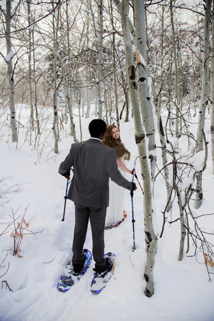 Bride and groom snowshoeing through the snow and trees.