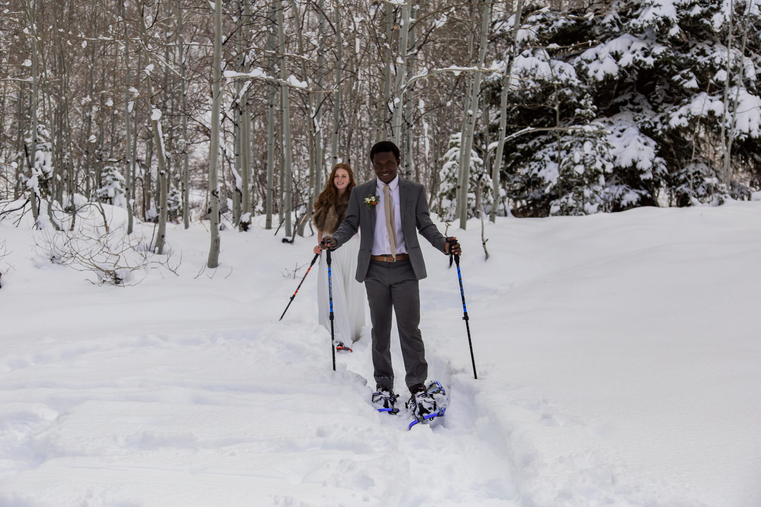 Bride and groom snowshoeing through the snow and trees.