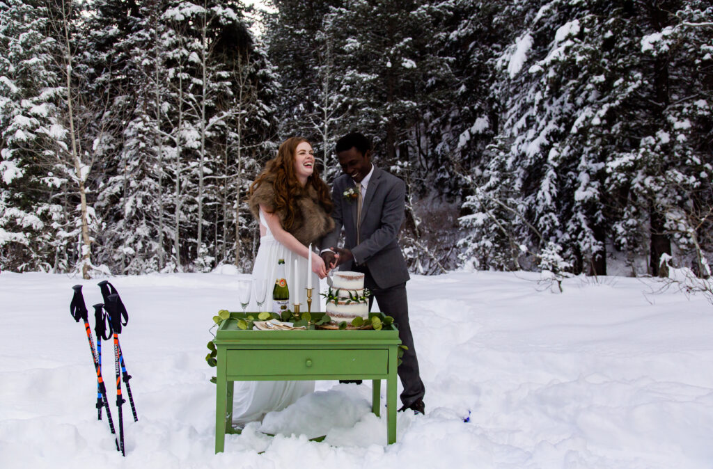 Bride and groom cutting cake during their snowy winter snowshoeing elopement.