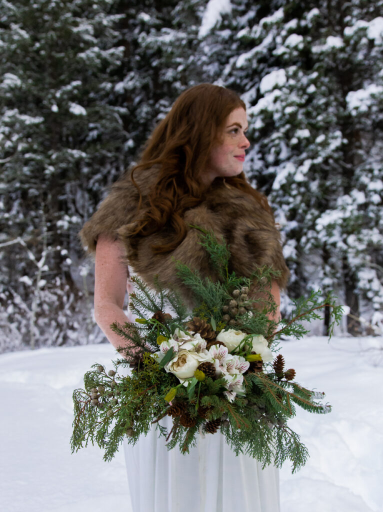 Bride by herself looking off at her groom holding winter bouquet in front of her.