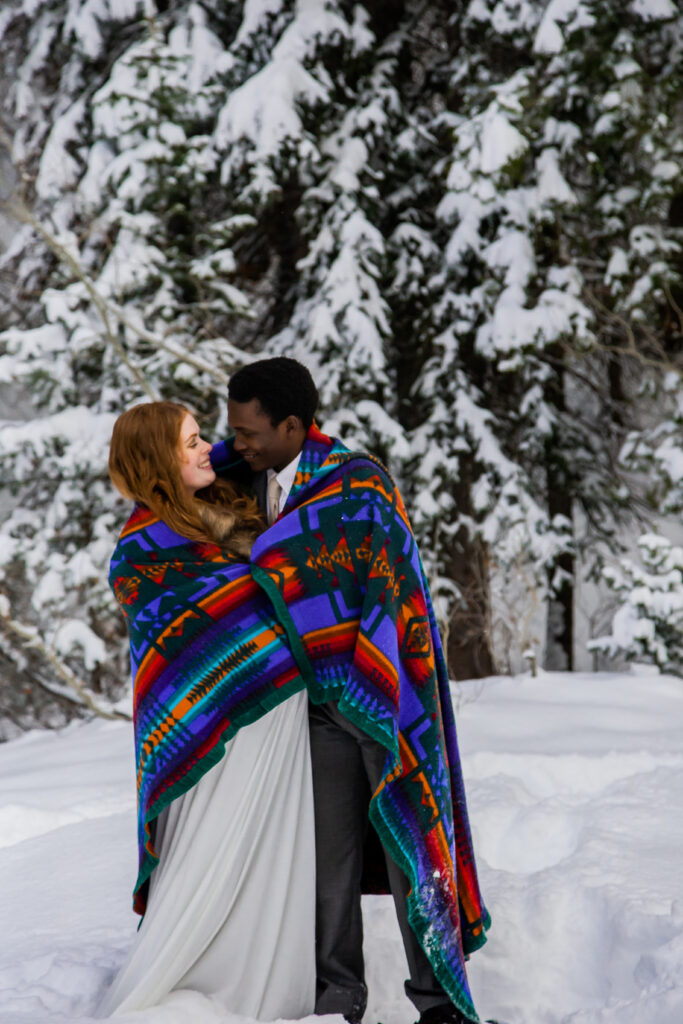 Bride and groom cuddling up together with blanket to keep warm.