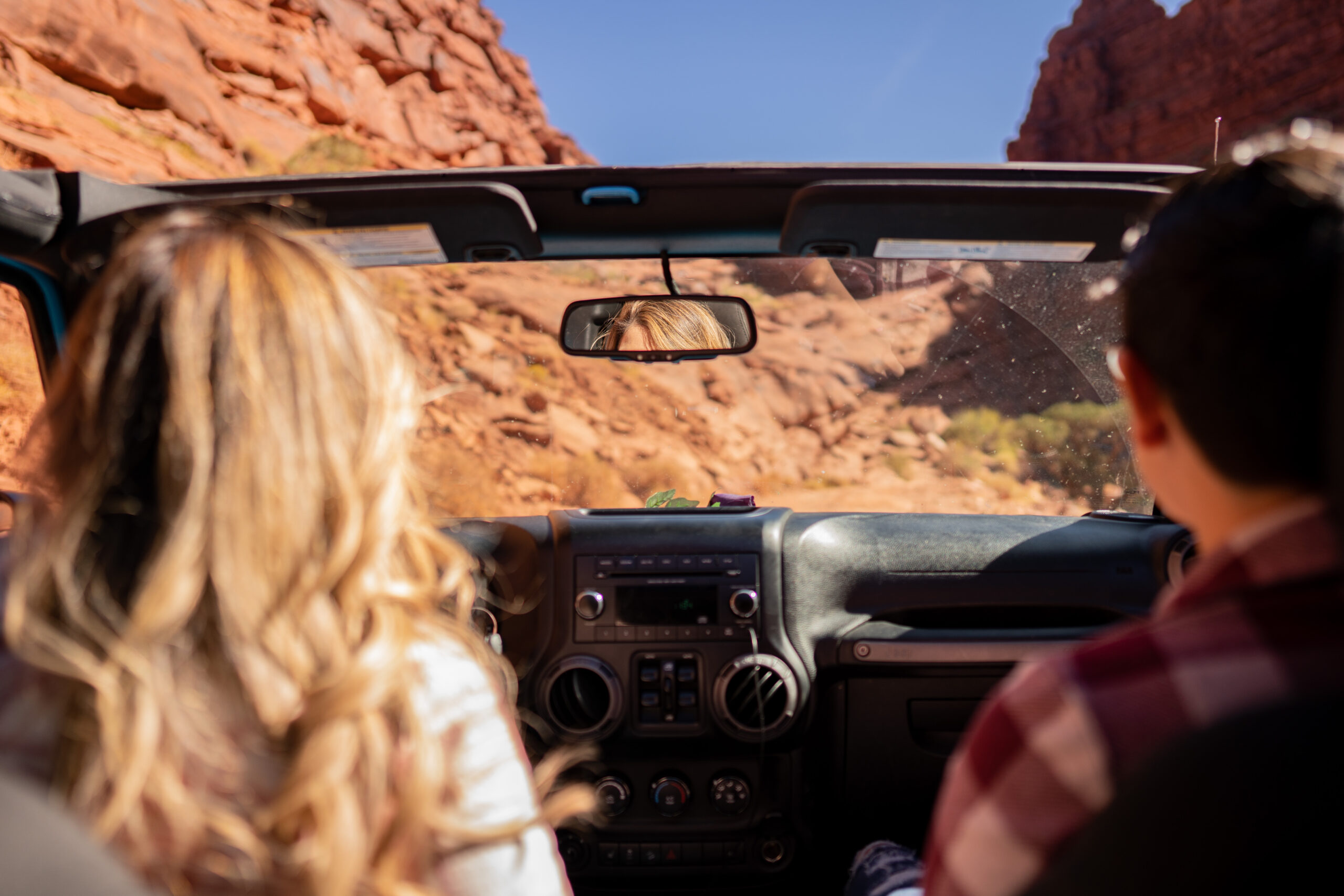 Two brides in a Jeep Wrangler with the top off, off roading through a red rock canyon in Moab, Utah