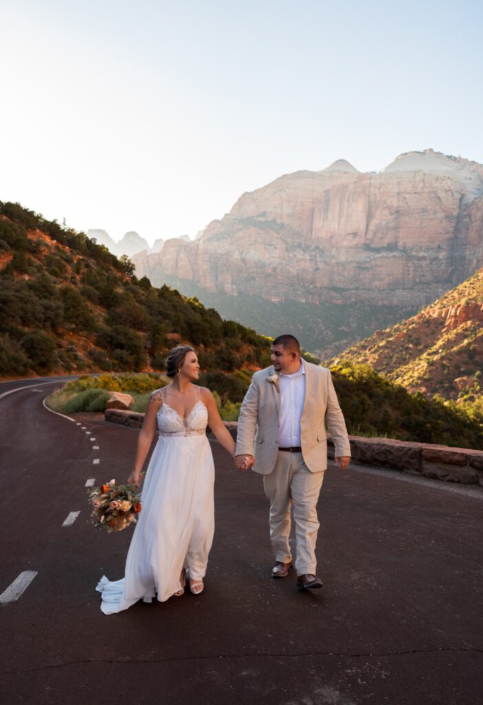 Bride and groom walking towards from the camera holding hands and looking at each other in Zion National Park in Utah