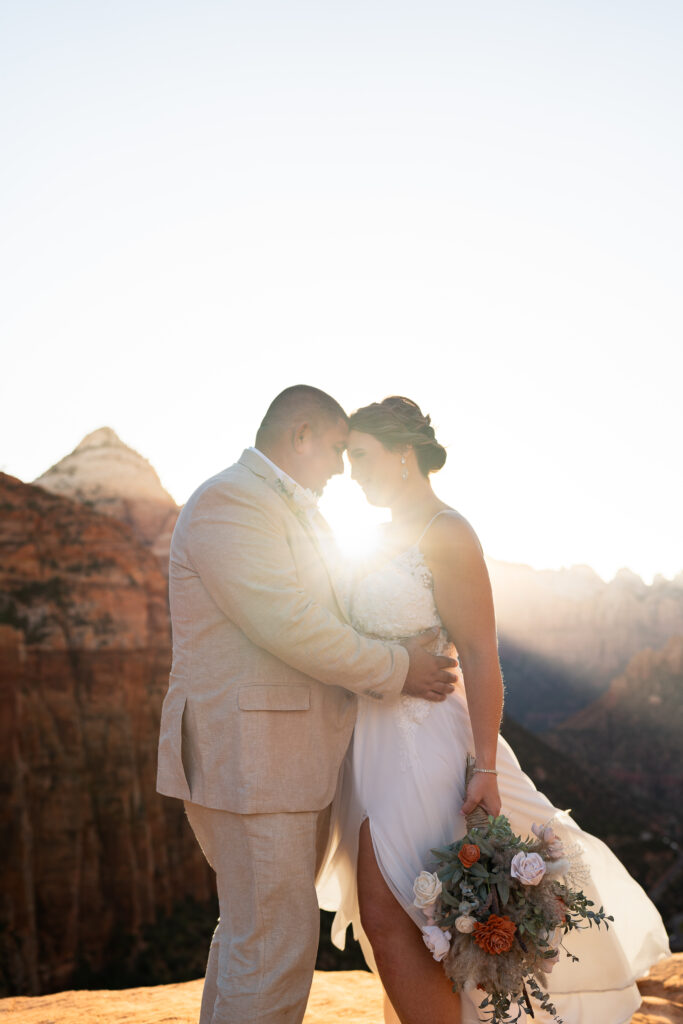 Bride and groom facing each other with their foreheads together and eyes closed on a cliff in Zion National Park in Utah