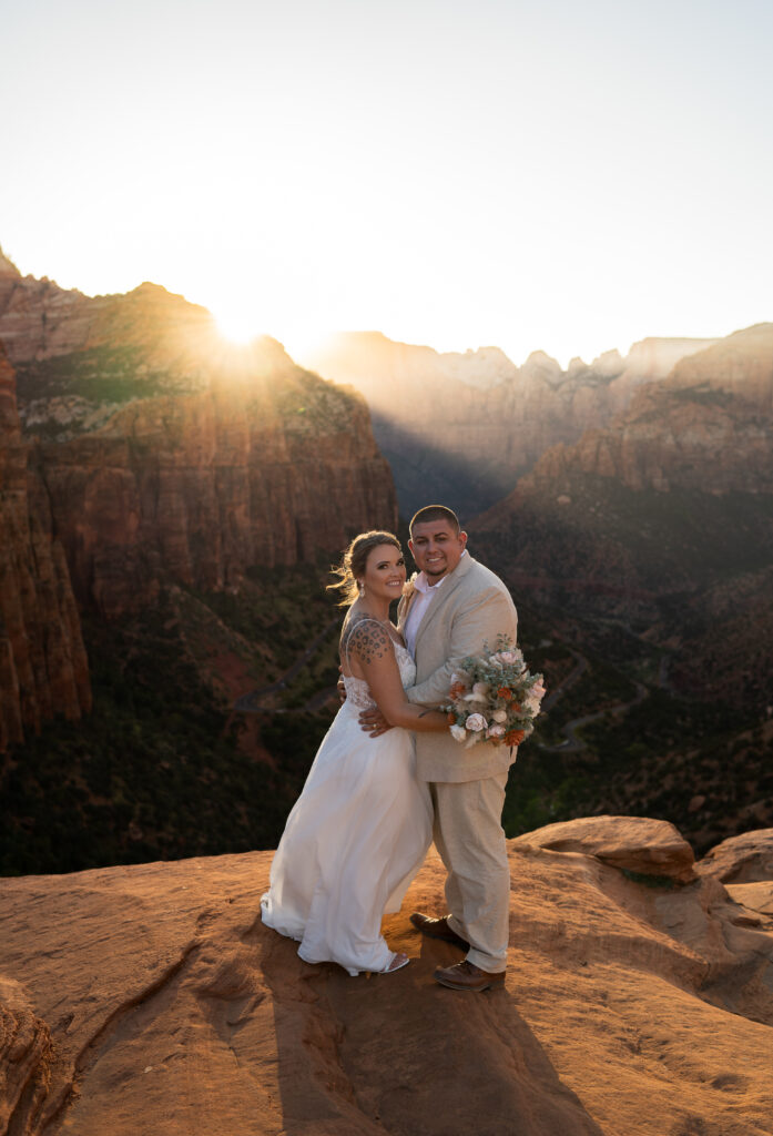 Bride and groom facing each other and smiling at the camera on a cliff in Zion National Park in Utah