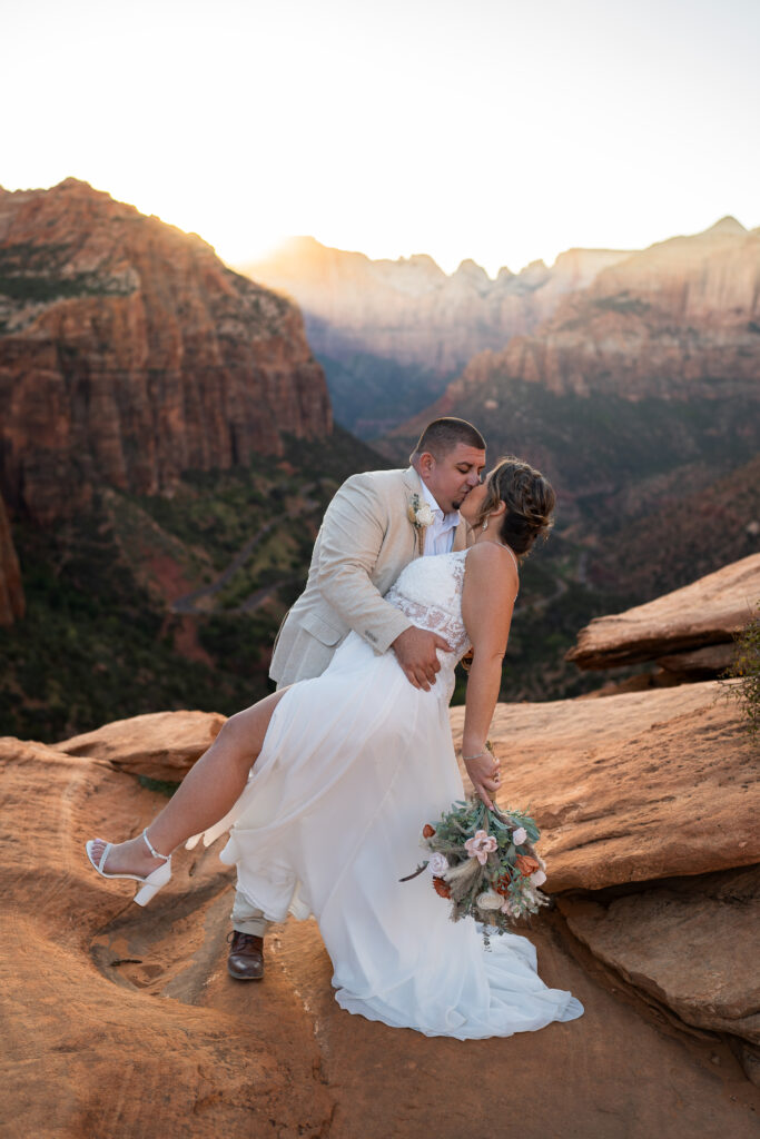 Groom dipping his bride and kissing on a cliff in Zion National Park in Utah