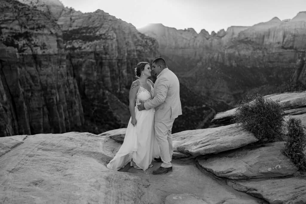 Bride and groom facing each other and going in for a kiss on a cliff in Zion National Park in Utah