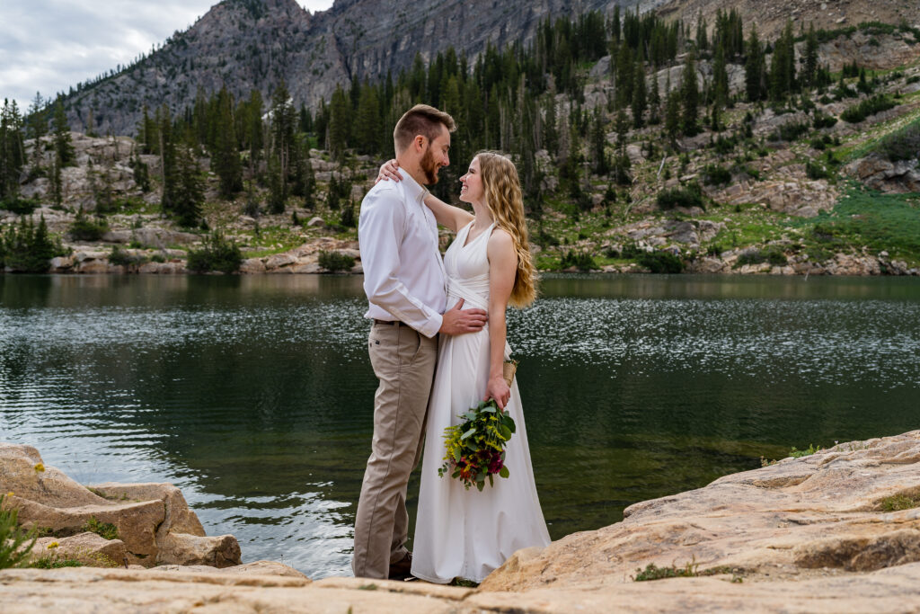 Bride and groom embracing each other in front of an alpine lake in the mountains near Salt Lake City, Utah