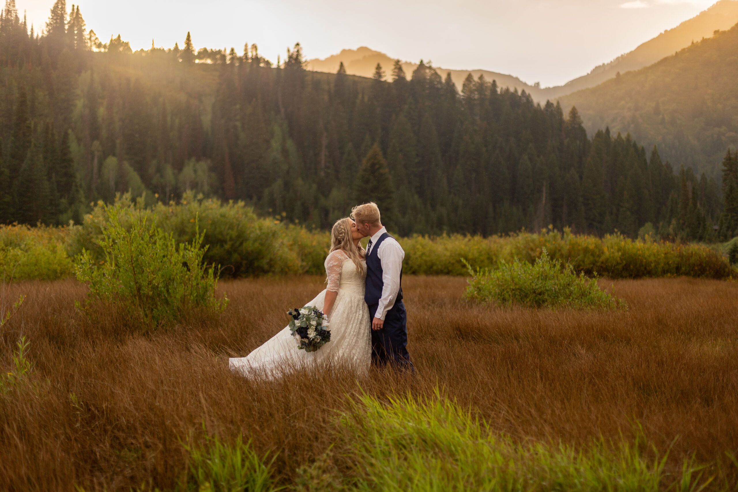 Bride and groom kidding in the middle of a meadow with the sun shining behind the mountains in Salt Lake City, Utah
