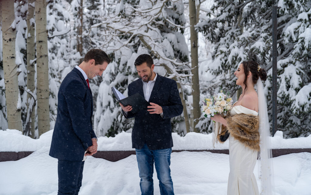Bride and groom laughing with their officiant during their snowy mountain elopement in Park City, Utah