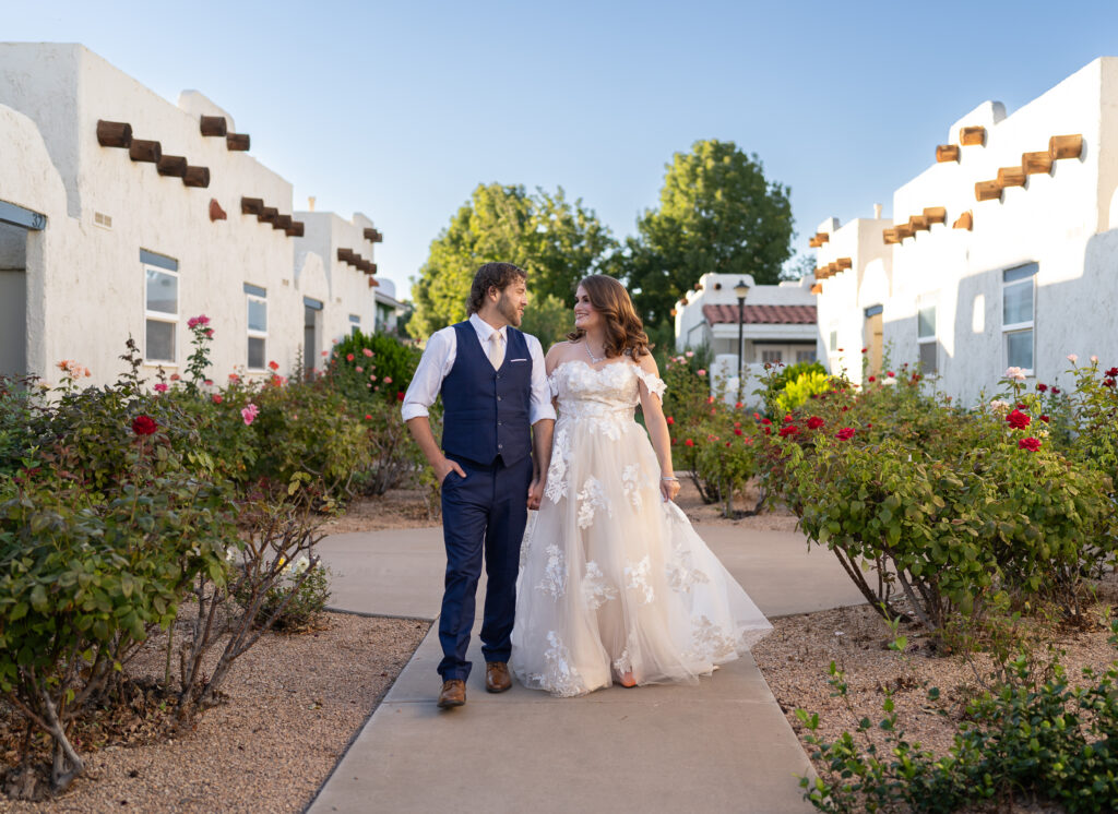 Bride and groom walking down sidewalk with roses and stucco homes on each side