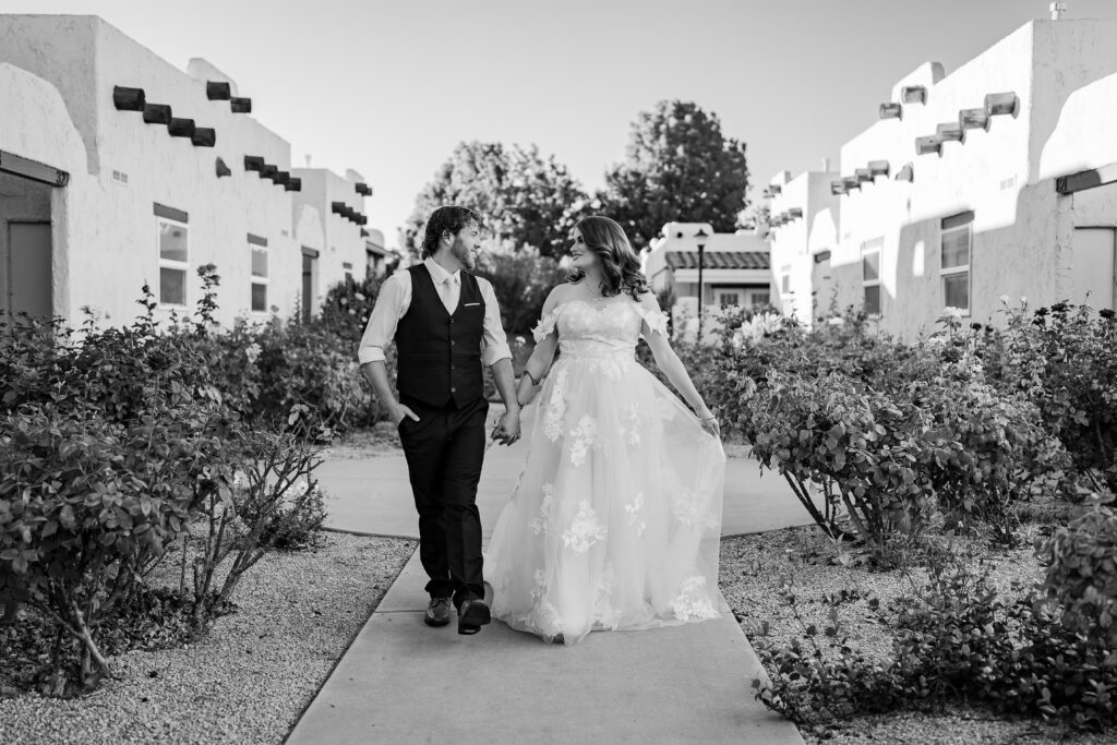 Bride and groom walking down sidewalk with roses and stucco homes on each side