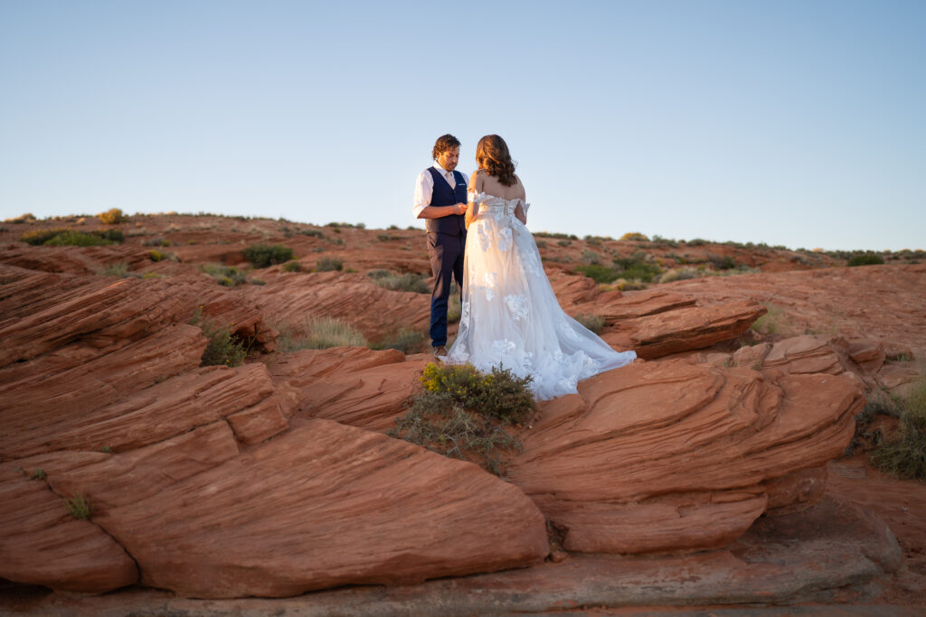 Bride and groom standing on red rock cliff reading vows o each other at sunset