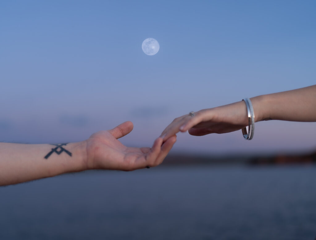 Bride and groom's hands with fingertips barely touching and the moon in the background