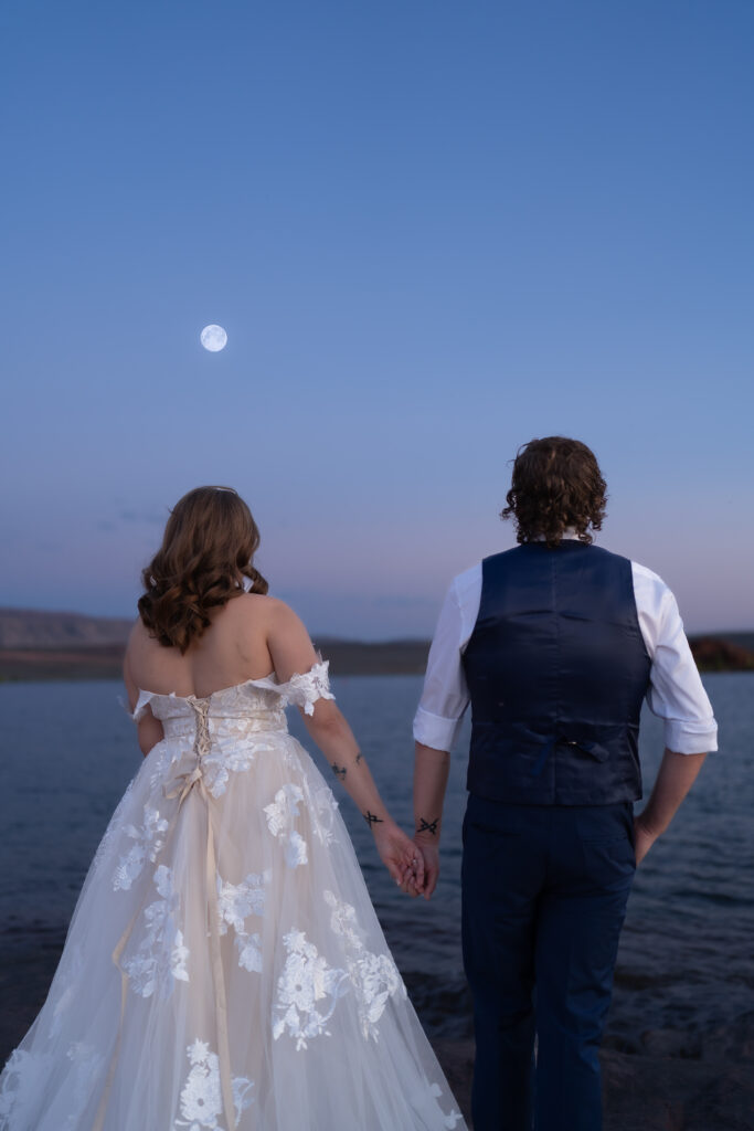 Bride and groom facing away from the camera holding hands and looking at the moon