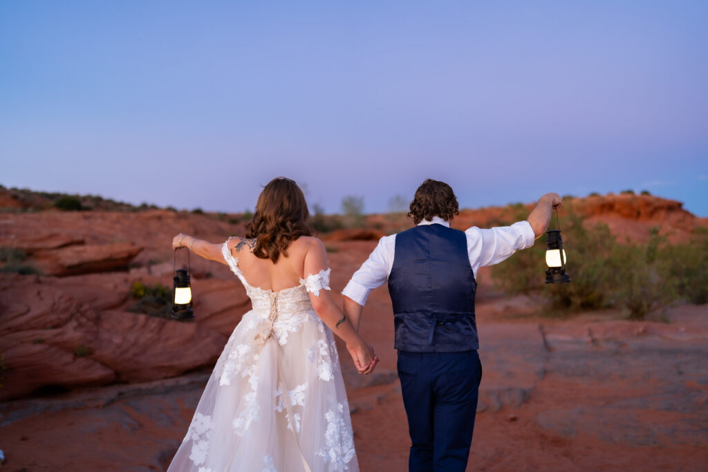 Bride and groom facing away from camera and walking while holding out their lanterns to the sides of them