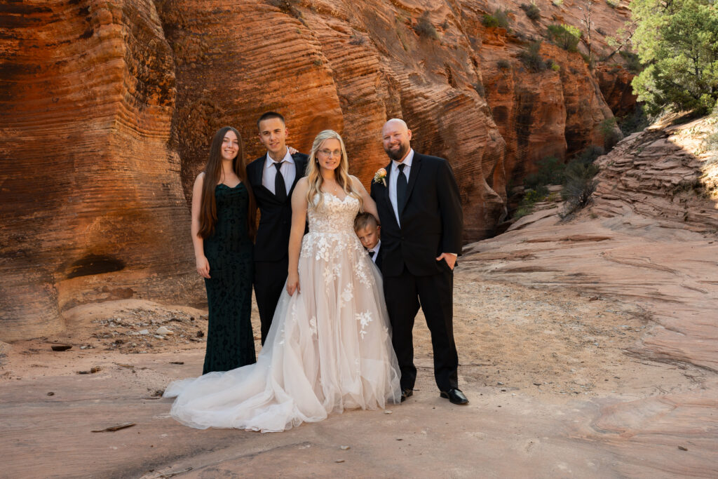 Bride and groom in their wedding attire with their children in a red rock slot canyon in Zion National Park in Utah