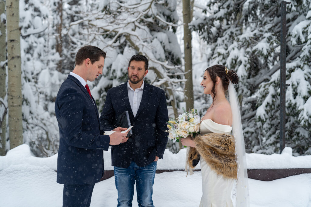 Groom reading his vows to the bride in a snowy winter scene with officiant watching in Park City, Utah