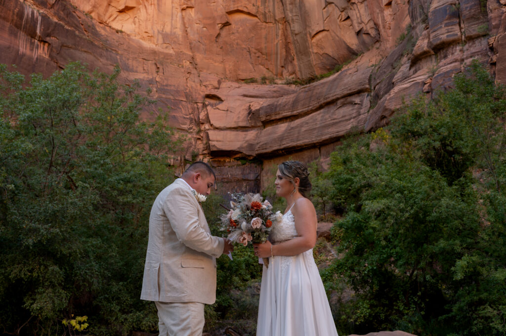 Groom reading his vows to the bride in a red rock wall behind them in Zion National Park in Utah.