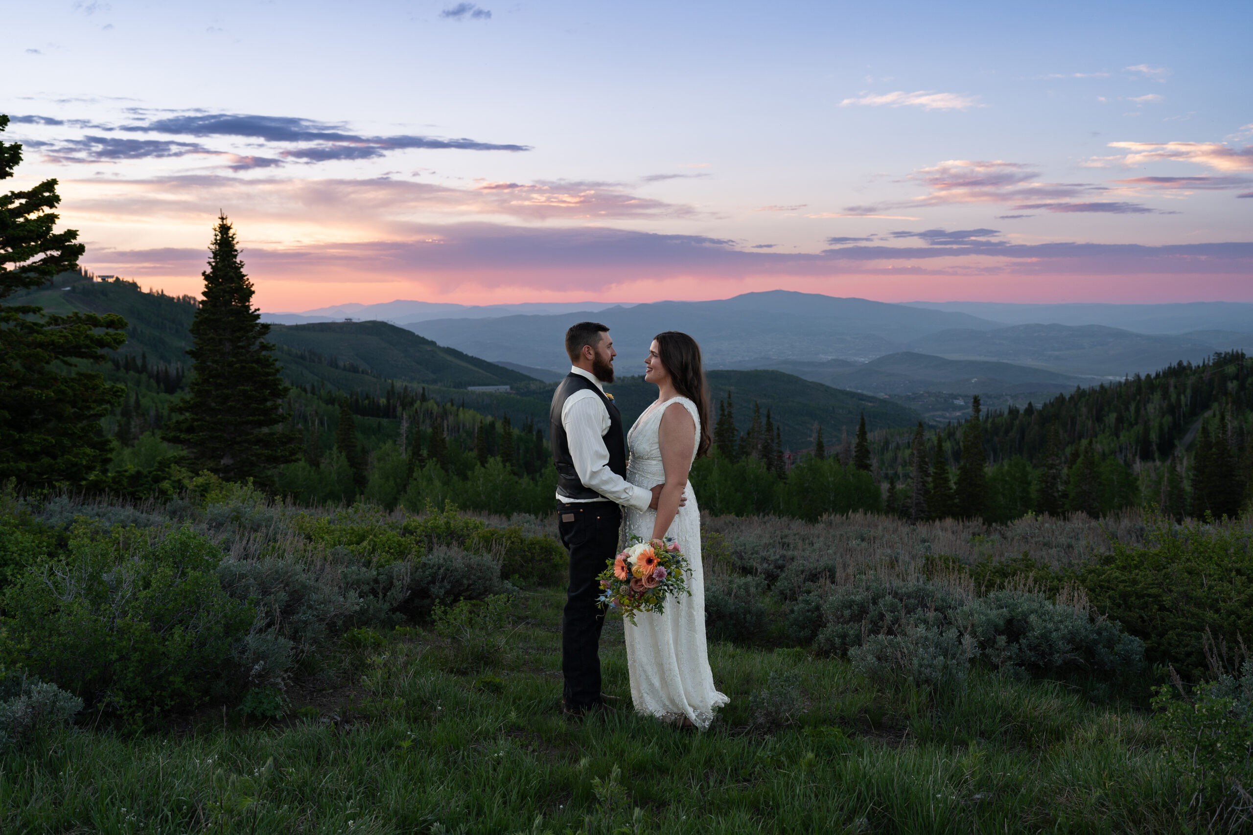 Eloping Bride and Groom standing together in front of lush green mountains at sunset in Park City, Utah