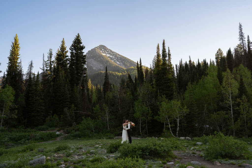 Eloping bride and groom with their arms around each other in front of a green summer mountain backdrop in Park City, Utah