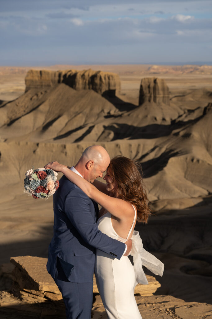 Bride has her arms draped over the groom's shoulders and they have their foreheads together, standing at Moonscape overlook outside of Capitol Reef National Park in Utah