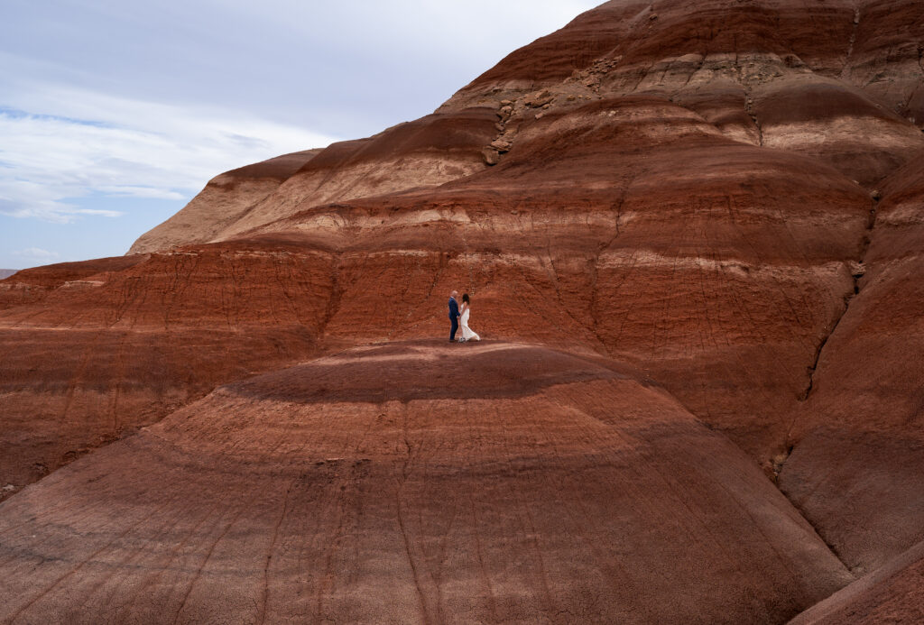 Bride and Groom facing each other holding hands on top on the Bentonite Hills in Hanksville, Utah, right outside of Capitol Reef National Park