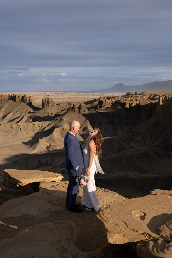 Bride and groom standing together laughing over the wind at Moonscape overlook, outside of Capitol Reef National Park in Utah